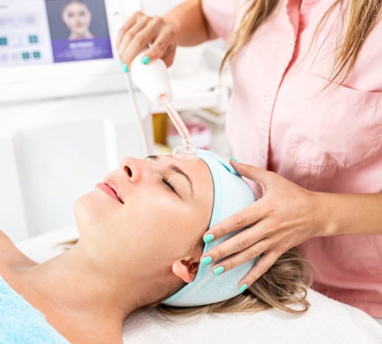Beautician therapist applying face treatment in beauty salon to young woman.