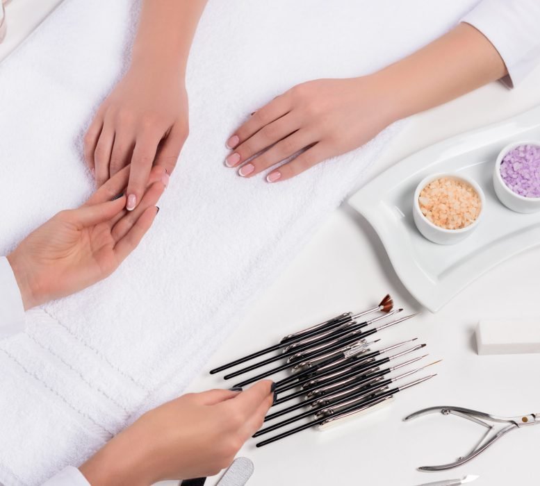 cropped shot of beautician doing manicure to woman at table with colorful sea salt, nail polishes,