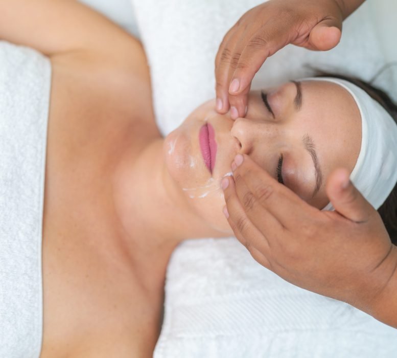 Top view close-up of a latin woman receiving a Facial peeling massage in a wellness spa