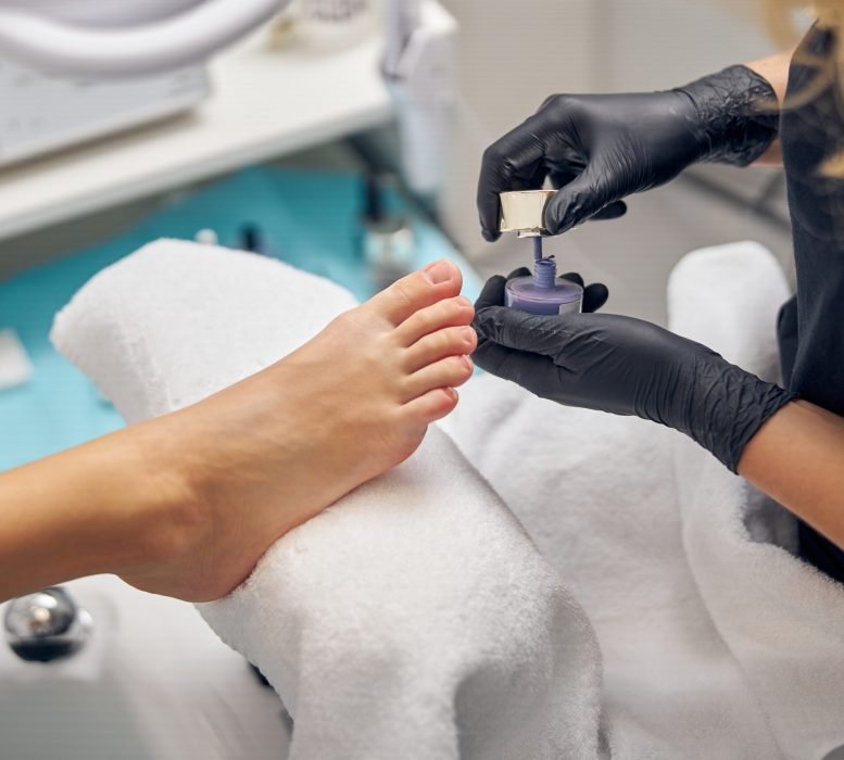 Top view close up of female foot while artist is holding bottle of cosmetic polish in beauty salon